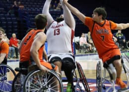 Alabama’s 13 lifts a shot over Auburn defenders in wheelchair basketball, with an orange Tigers player reaching in from the right.