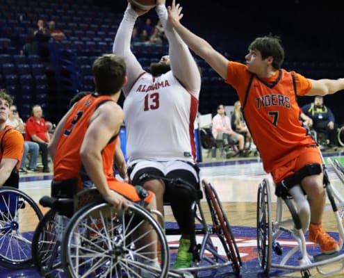 Alabama’s 13 lifts a shot over Auburn defenders in wheelchair basketball, with an orange Tigers player reaching in from the right.