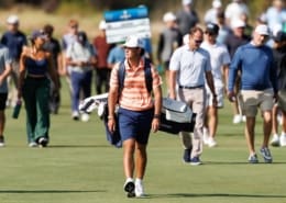 Jackson Koivun walks across a golf course in an orange-striped Auburn polo with a white cap and a bag on his back.